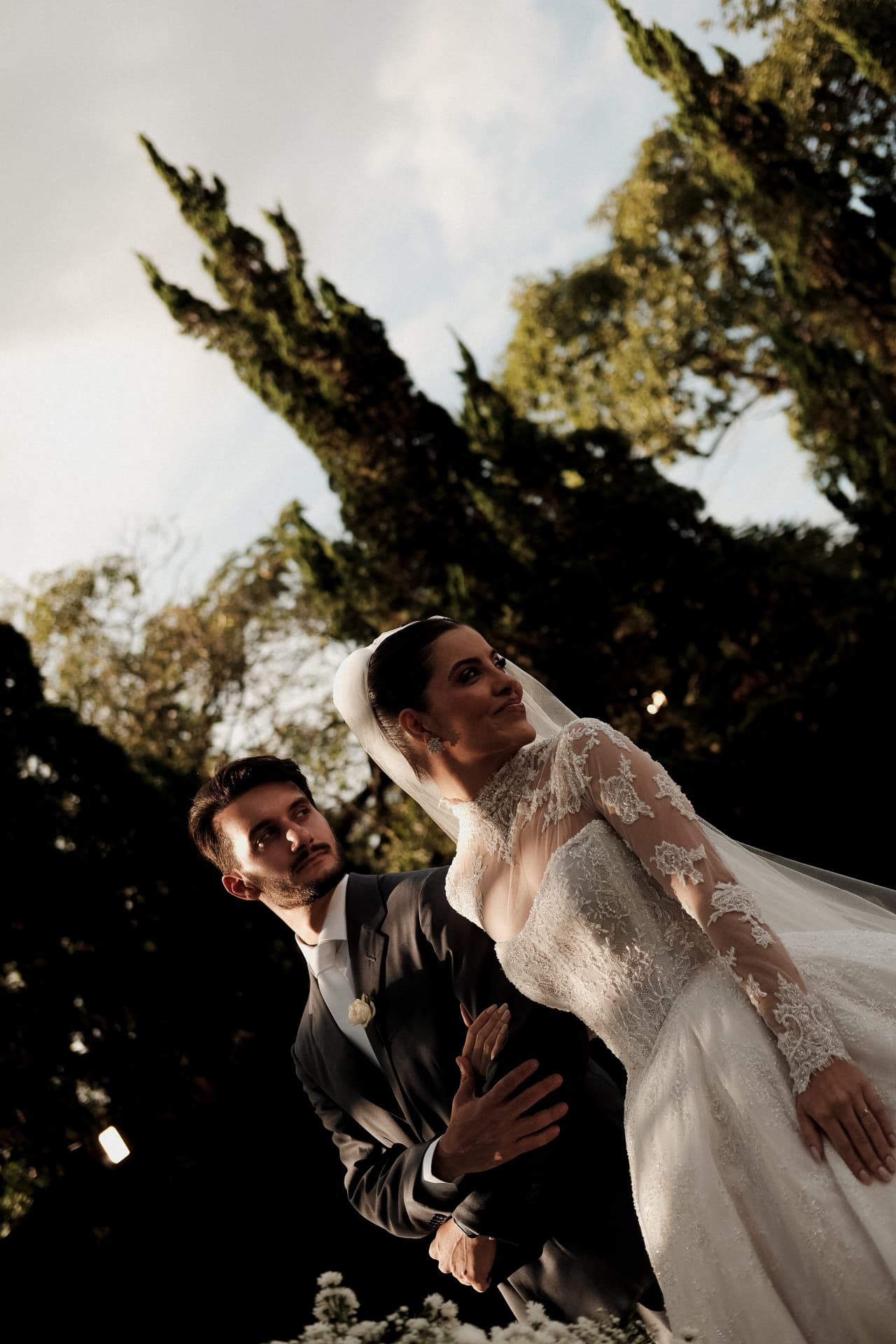 Casal com véu ao vento sob as árvores